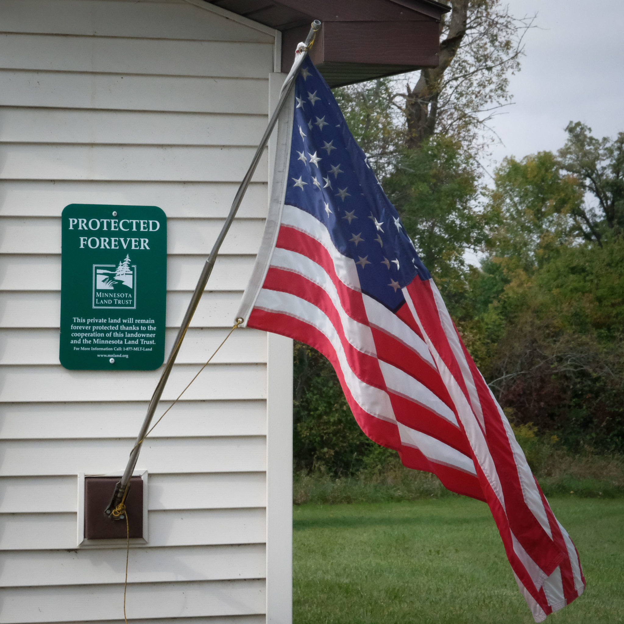 American flag flying next to a Minnesota Land Trust Protected Forever sign