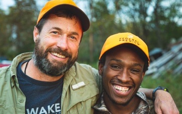 Two men wearing orange hats smiling for a photo