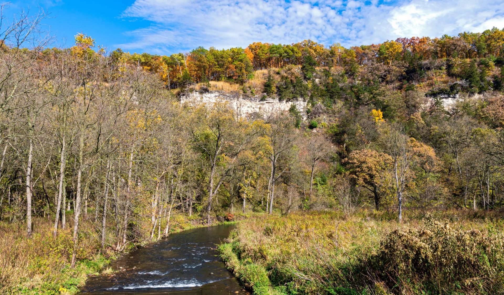 A stream with fall colored trees atop a bluff in the background