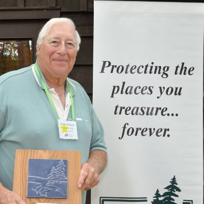 A man smiles for the camera and holds an award plaque next to a banner that reads "Protecting the places you treasure...forever"