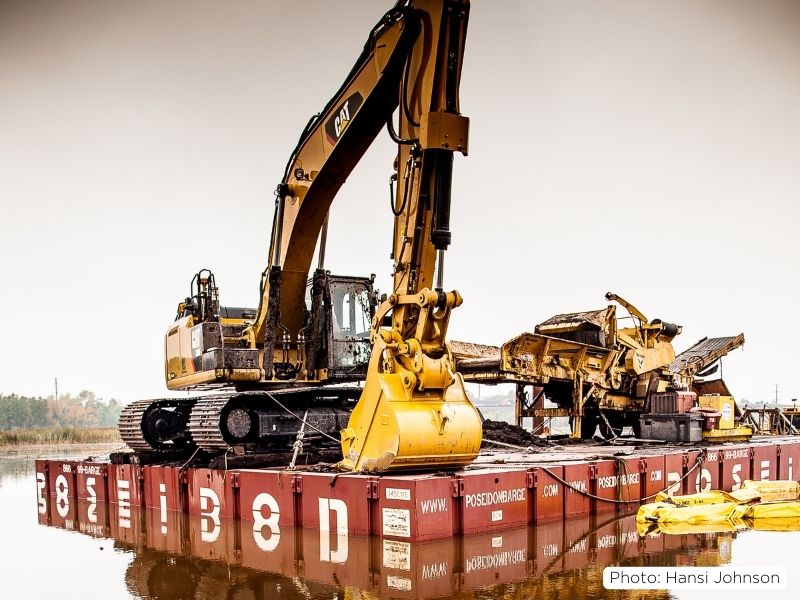 A photo of construction equipment used to excavate the debris from the bottom of the bay sitting on a barge/float.