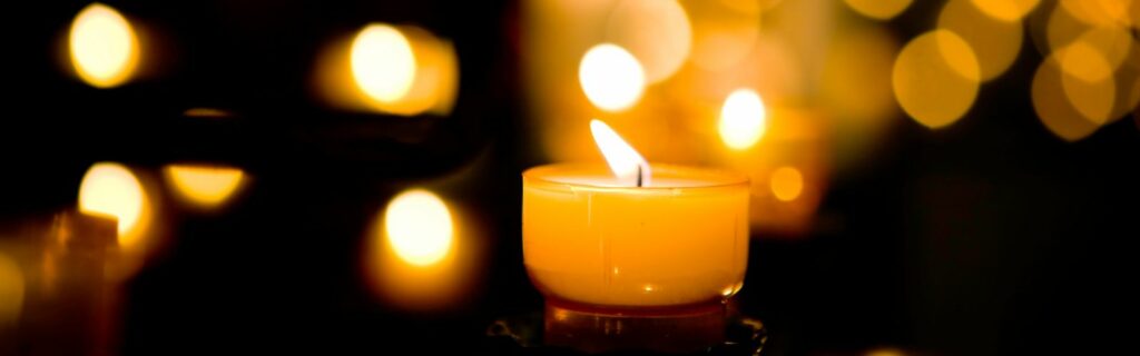 White candle lit in the foreground with candles and white lights in background